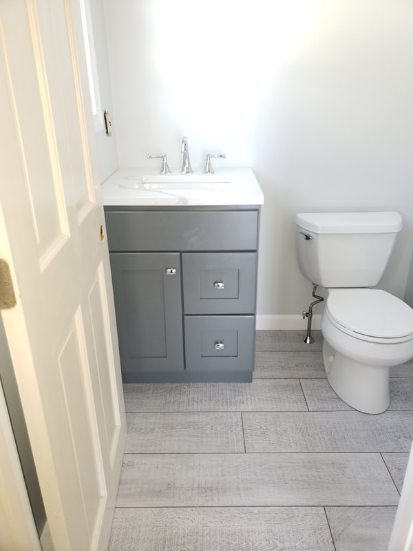 bathroom remodel after gray storage vanity, silver faucet, white marble look sink and toilet installation