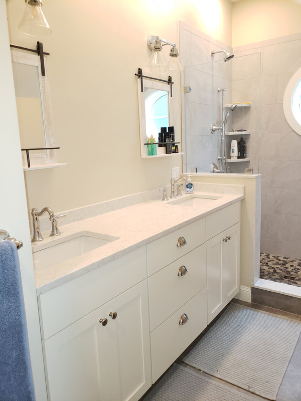 House remodel project with second finished bathroom. Double sink white vanity with storage, two above sink mirrors with shelf, and walk in shower with dual shower heads.