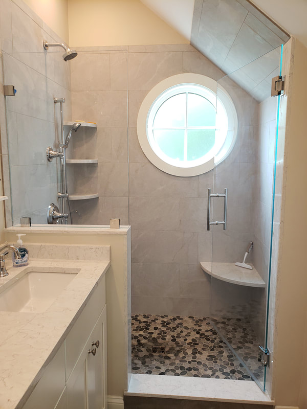 Home remodel project with second finished bathroom. Walk in shower with dual shower heads, built in corner shelving, built in corner seat and glass door. Round window accent inside shower.